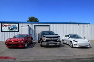 Three vehicles displayed outside a dealership: red sports car, dark pickup truck, and white sedan, with showroom building in background