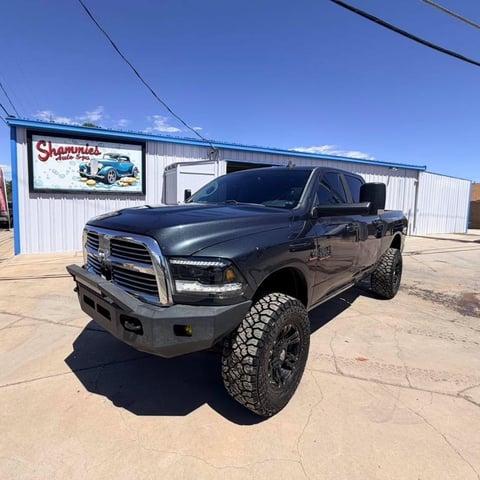 Black lifted Dodge Ram pickup truck with large tires parked outside a shop on a sunny day
